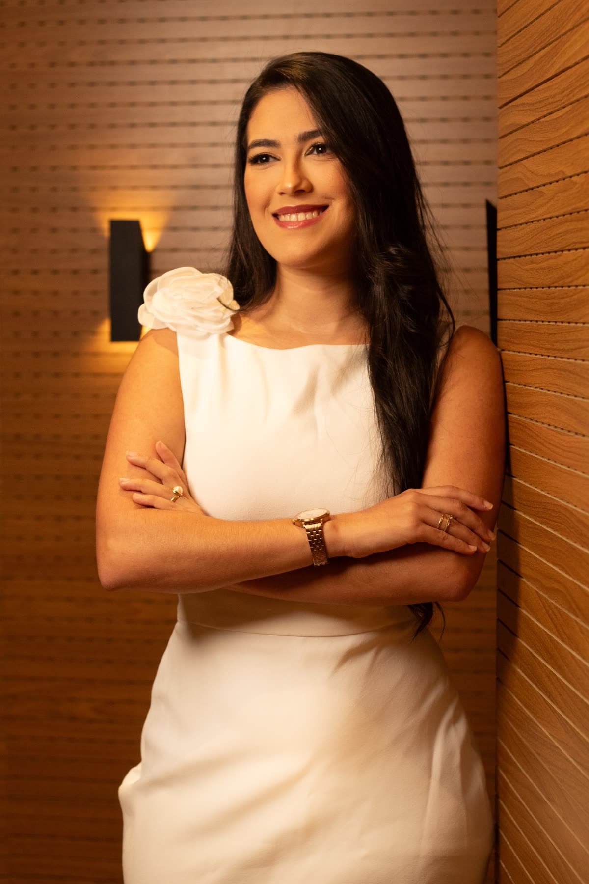 Lígia Ferreira sorrindo, de braços cruzados, encostada no painel de madeira do escritório